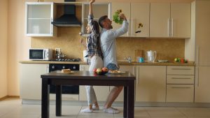 Attractive young joyful couple have fun dancing and singing while cooking in the kitchen at home in the morining