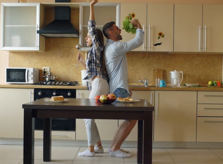 Attractive young joyful couple have fun dancing and singing while cooking in the kitchen at home in the morining